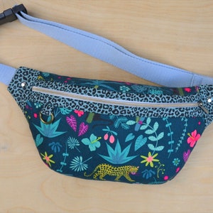 May include: A teal blue fanny pack with a zipper closure and a leopard print trim. The main fabric features a tropical print with green leaves, pink flowers, and a yellow leopard.