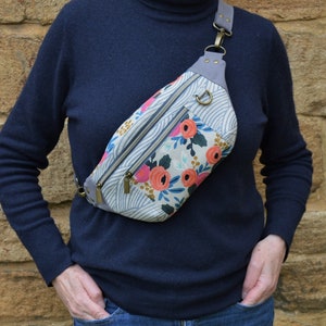 May include: A floral patterned fanny pack with a gray strap and a silver buckle. The bag has a zippered pocket and a flap closure.
