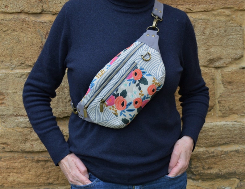 May include: A floral patterned fanny pack with a gray strap and a silver buckle. The bag has a zippered pocket and a flap closure.
