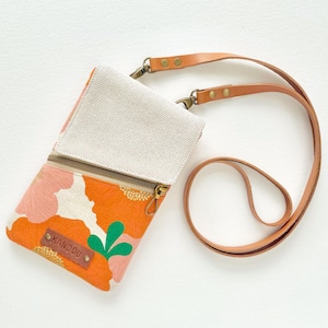 Puede incluir: Bolso bandolera con estampado floral, parte superior de lona beige y correa de cuero marr&oacute;n. El bolso presenta un vibrante estampado floral naranja y rosa, una cremallera dorada y el texto "KANDOU" en una etiqueta de cuero marr&oacute;n.