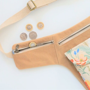 Pu&ograve; includere: Una cintura in tela beige con una tasca con cerniera e una borsa con stampa floreale. La cintura ha una cinghia e una chiusura a fibbia. Ci sono diverse monete britanniche nella tasca con cerniera.