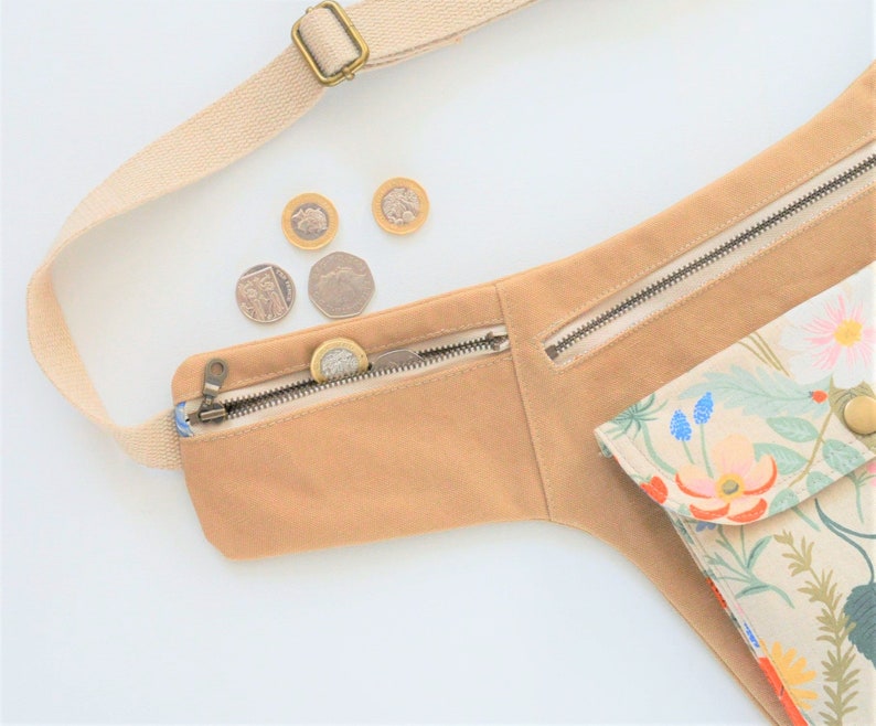 Pu&ograve; includere: Una cintura in tela beige con una tasca con cerniera e una borsa con stampa floreale. La cintura ha una cinghia e una chiusura a fibbia. Ci sono diverse monete britanniche nella tasca con cerniera.