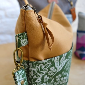 May include: A mustard yellow canvas zippered pouch with a green floral print on the bottom half. The pouch has a brown leather zipper pull and a gold metal key chain.