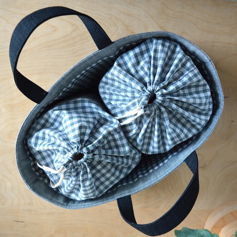 May include: A denim tote bag with black handles, containing two drawstring bags. The drawstring bags are made of a green and white checkered fabric. The tote bag is open, showing the contents inside.