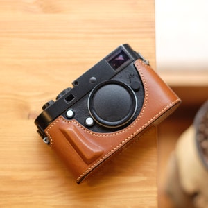 May include: A black camera with a brown leather case. The camera has a lens cap and a viewfinder.