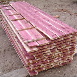 May include: A stack of cedar wood planks, showing the natural reddish-brown color of the wood. The planks are stacked neatly and are ready for use in a variety of woodworking projects.