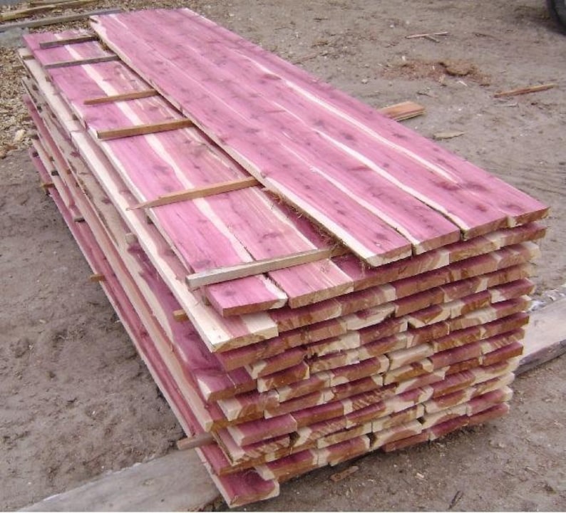 May include: A stack of cedar wood planks, showing the natural reddish-brown color of the wood. The planks are stacked neatly and are ready for use in a variety of woodworking projects.