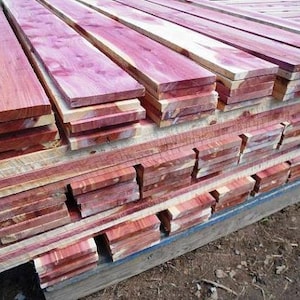 May include: A stack of cedar wood planks, with a reddish-brown hue, are stacked and ready for use in a woodworking project.