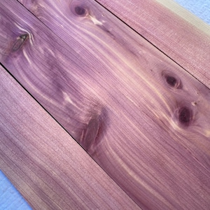 May include: Four pieces of wood with a purple hue and a natural wood grain pattern. The wood has knots and a light brown color in some areas.