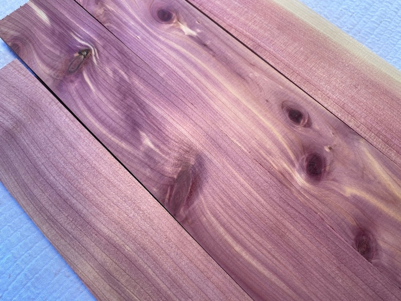 May include: Four pieces of wood with a purple hue and a natural wood grain pattern. The wood has knots and a light brown color in some areas.