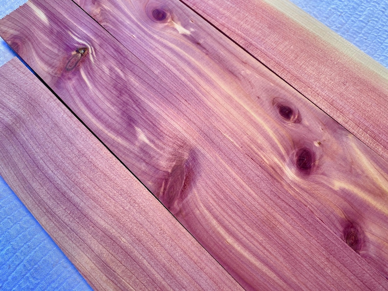 May include: Close-up of four pieces of cedar wood with a reddish-purple hue and a natural wood grain pattern. The wood has a smooth surface and is arranged in a diagonal pattern.