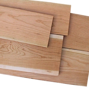 以下が含まれることがあります： 異なる木目模様の、未仕上げの桜材が4枚。木の色は薄い茶色で、表面は滑らかです。