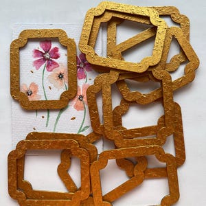 May include: A set of ten gold-coloured metal frames with a textured surface. The frames are all the same size and shape, and they have a scalloped edge.