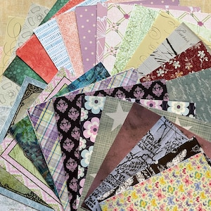 May include: A selection of patterned scrapbook paper in various colours and designs. The papers feature floral, plaid, and abstract patterns. The colour palette includes pinks, greens, blues, and purples. The papers are arranged in a fan shape.