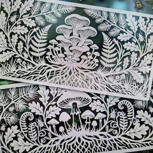 May include: Two white, rectangular laser-cut designs with detailed botanical and mushroom illustrations. The designs feature ferns, oak leaves, and various mushroom species, with a root-like base. The overall theme is nature and the forest, with a focus on intricate detail.