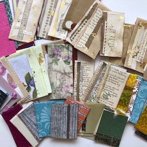 May include: A collection of small, rectangular paper scraps with various patterns, textures, and colours. Some scraps have gold leaf accents, while others have handwritten text. The scraps are arranged on a white surface.