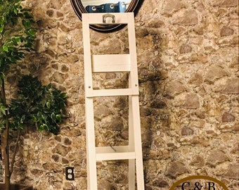 May include: White wooden ladder shelf with four shelves. The shelf is standing in front of a stone wall with a round mirror above it. The text "C&B designs" is visible in the lower right corner of the image.