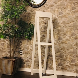 May include: White wooden A-frame display stand with two shelves. The stand is in front of a stone wall with a mirror above it.