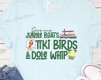 May include: A light blue t-shirt with the text "Give me Jungle Boats Tiki Birds & Dole Whip" in green and white lettering. The shirt features a cartoon image of a boat, a bird, and a Dole Whip.