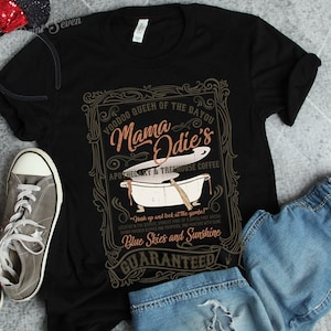 May include: Black t-shirt with a vintage-style graphic design featuring a bathtub and the text "Voodoo Queen of the Bayou Mama Odie's Apothecary & Treehouse Coffee". The text "Y'all come on up and lock at the gumbo!" is also included. The graphic is surrounded by a decorative frame.