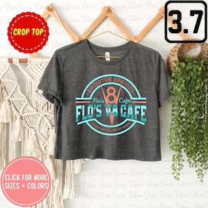 May include: A gray crop top with a vintage-style logo that reads "RADIATOR SPRINGS - Flo's Cafe - FLO'S V8 CAFE -  BURGERS - GAS - OIL - COOLANT - SERVICE".