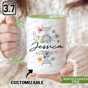 May include: White ceramic mug with a green handle and interior. The mug features a floral design with a DNA strand and the name "Jessica". The mug is customizable and holds 15 ounces.