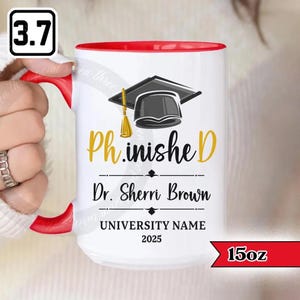 May include: White ceramic mug with a red interior and handle. The mug features the text "Ph.inished" in gold, a graduation cap graphic, and the name "Dr. Sherri Brown". The mug is 15oz.