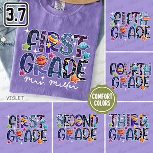 May include: A violet Comfort Colors t-shirt with a colorful "First Grade" design featuring planets, stars, and the name "Mrs. Miller." Additional shirts show "Second," "Third," "Fourth," and "Fifth Grade" designs.