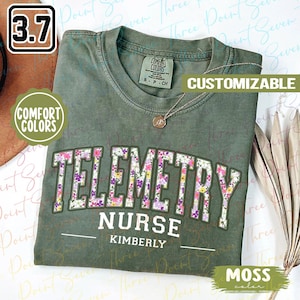 May include: A green t-shirt with a floral design that says "Telemetry Nurse Kimberly" in white text. The shirt is customizable and has a moss color.