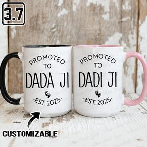 Op de afbeelding: Twee witte keramische mokken met zwarte en roze accenten. Elke mok heeft de tekst "PROMOTED TO DADA JI" en "PROMOTED TO DADI JI" in het zwart, met "EST. 2025" eronder. De mokken zijn aanpasbaar.