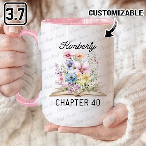 May include: White ceramic mug with a pink interior and handle, featuring a floral design and the name "Kimberly." The mug also displays "Chapter 40." The mug is held by a person.