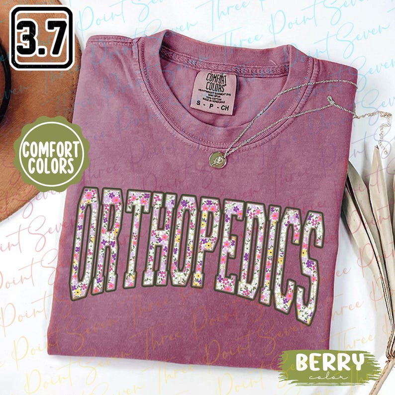 May include: A mauve t-shirt with a floral print design that says "ORTHOPEDICS" in a white outline. The shirt is made by Comfort Colors and has a tag that says "S - P - CH".
