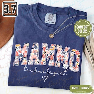 May include: A navy blue t-shirt with the word "MAMMO" in large floral letters. Below it, the word "technologist" is written in script, with a heart symbol. The shirt has a Comfort Colors tag.