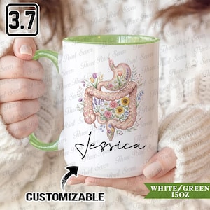 Peut inclure: Mug en céramique blanche avec une anse et un intérieur verts. La tasse présente une illustration florale du système digestif avec le nom "Jessica" en cursive. La tasse est étiquetée "Personnalisable" et "Blanc/Vert 15oz".