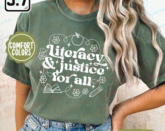 May include: Moss green t-shirt with the text "Literacy & Justice for All" in white, surrounded by floral and apple graphics. The shirt has a crew neck and short sleeves. The words "Comfort Colors" are printed on a circular label.