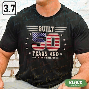 May include: Black t-shirt with a patriotic design. The graphic features the text "BUILT 50 YEARS AGO LIMITED EDITION" with the number 50 filled with the American flag. White stars and stripes complete the design.