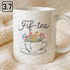May include: White ceramic mug with the text "Fif-tea" in a script font. The mug features a line drawing of a teacup filled with colorful flowers. A small tag hangs from the teabag. The mug has a white handle.