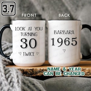 May include: White ceramic mug with a black handle and rim. The front of the mug says "LOOK AT YOU TURNING 30 TWICE" in black text. The back says "BARBARA 1965". The text "NAME & YEAR CAN BE CHANGED" is also visible.