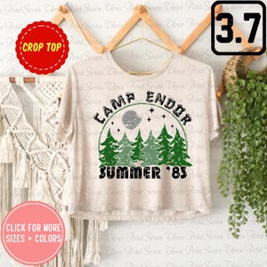 May include: A white crop top with a green and black graphic print that says "Camp Endor Summer '83". The graphic features a circle with a moon, stars, and pine trees.