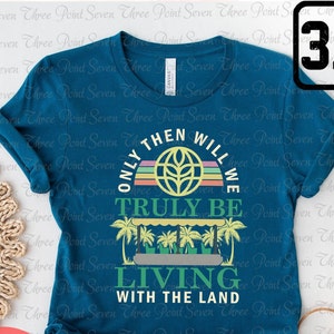 Op de afbeelding: Tealblauw T-shirt met een grafisch ontwerp van een wereldbol met een tarwehalm en de tekst "Only then will we truly be living with the land".