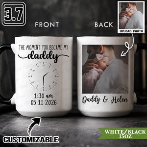 Op de afbeelding: Witte keramische mok met een zwarte handgreep en rand. De voorkant heeft de tekst "The moment you became my daddy" en een klokontwerp met de tijd 1:30 uur en de datum 05.11.2026. De achterkant toont een foto en de tekst "Daddy & Helen".