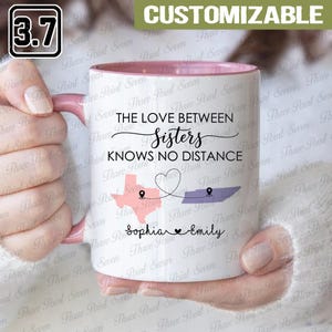 May include: White ceramic mug with a pink interior and handle. The mug features the text "THE LOVE BETWEEN SISTERS KNOWS NO DISTANCE" with a heart and two state outlines. The names "Sophia" and "Emily" are also printed on the mug.