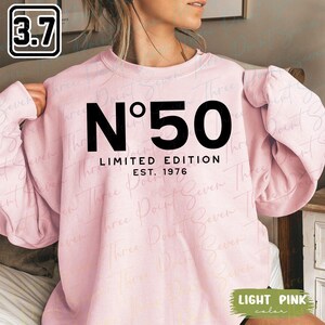 May include: Light pink sweatshirt with the text "N°50 LIMITED EDITION EST. 1976" in black. The sweatshirt has long sleeves and a crew neck. The color is described as "LIGHT PINK".