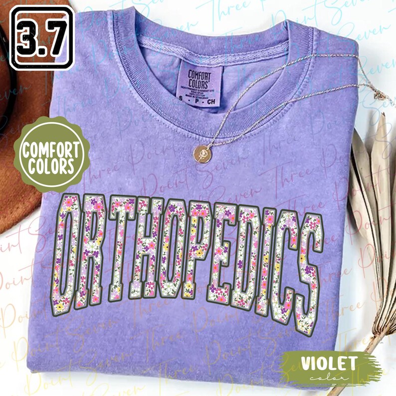 May include: A purple t-shirt with the word "ORTHOPEDICS" printed in white letters with a floral pattern. The shirt is made by Comfort Colors and is available in a violet color.