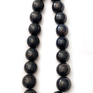 May include: A necklace featuring large, round beads in shades of dark blue and black with a speckled, metallic gold pattern. The beads are strung together with a silver clasp, creating a striking jewelry piece.