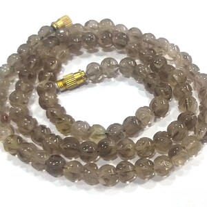 May include: A strand of smoky quartz beads with a carved design. The beads are a light brown colour and are strung on a gold cord.