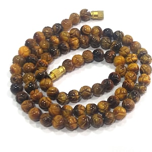 May include: A brown and gold tiger's eye beaded necklace with carved beads. The necklace has a gold clasp.