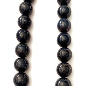 May include: A necklace featuring large, round, dark blue beads with gold flecks. The beads are strung together with a silver clasp. The necklace is displayed against a white background.