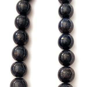 May include: A necklace featuring large, round beads in a dark blue color with gold flecks. The beads are strung together with a silver clasp. The necklace is displayed against a white background.