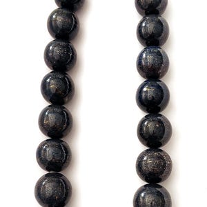 May include: A necklace featuring large, round beads in a dark navy blue color with gold flecks. The beads are strung together with a silver clasp. The necklace is displayed against a white background.